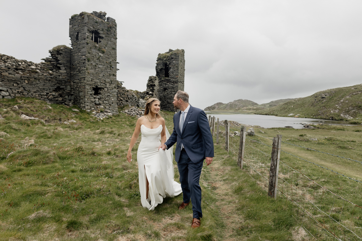 Groom adjusting his suit with castle ruins and ocean views at Mizen Head elopement location in County Cork, Ireland.