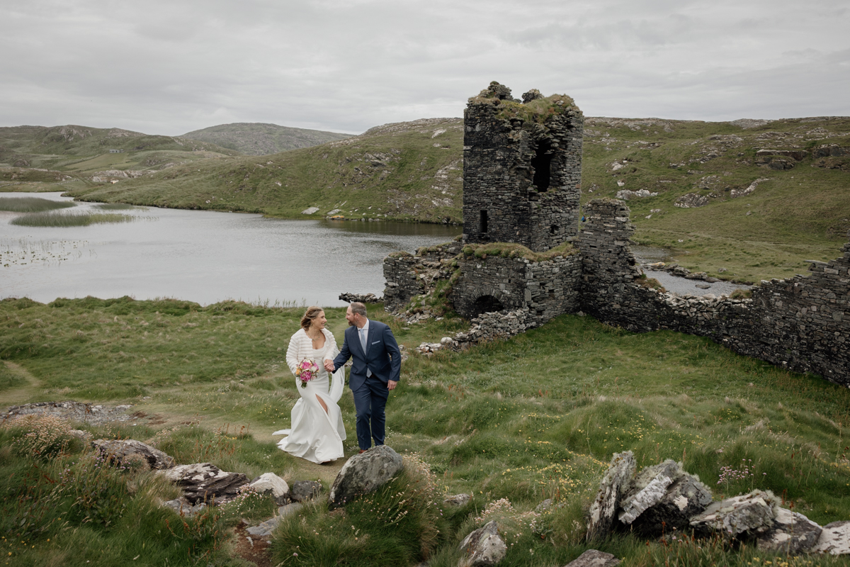 Couple embracing on the dramatic cliffs of Mizen Head, Ireland, with Three Castle Head ruins in the background.