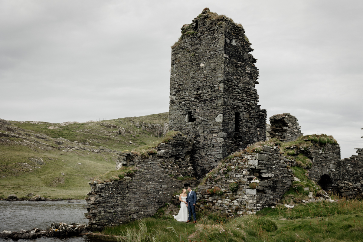 Windswept bride with veil at Three Castle Head ruins, perfect backdrop for adventurous couples eloping in Ireland.