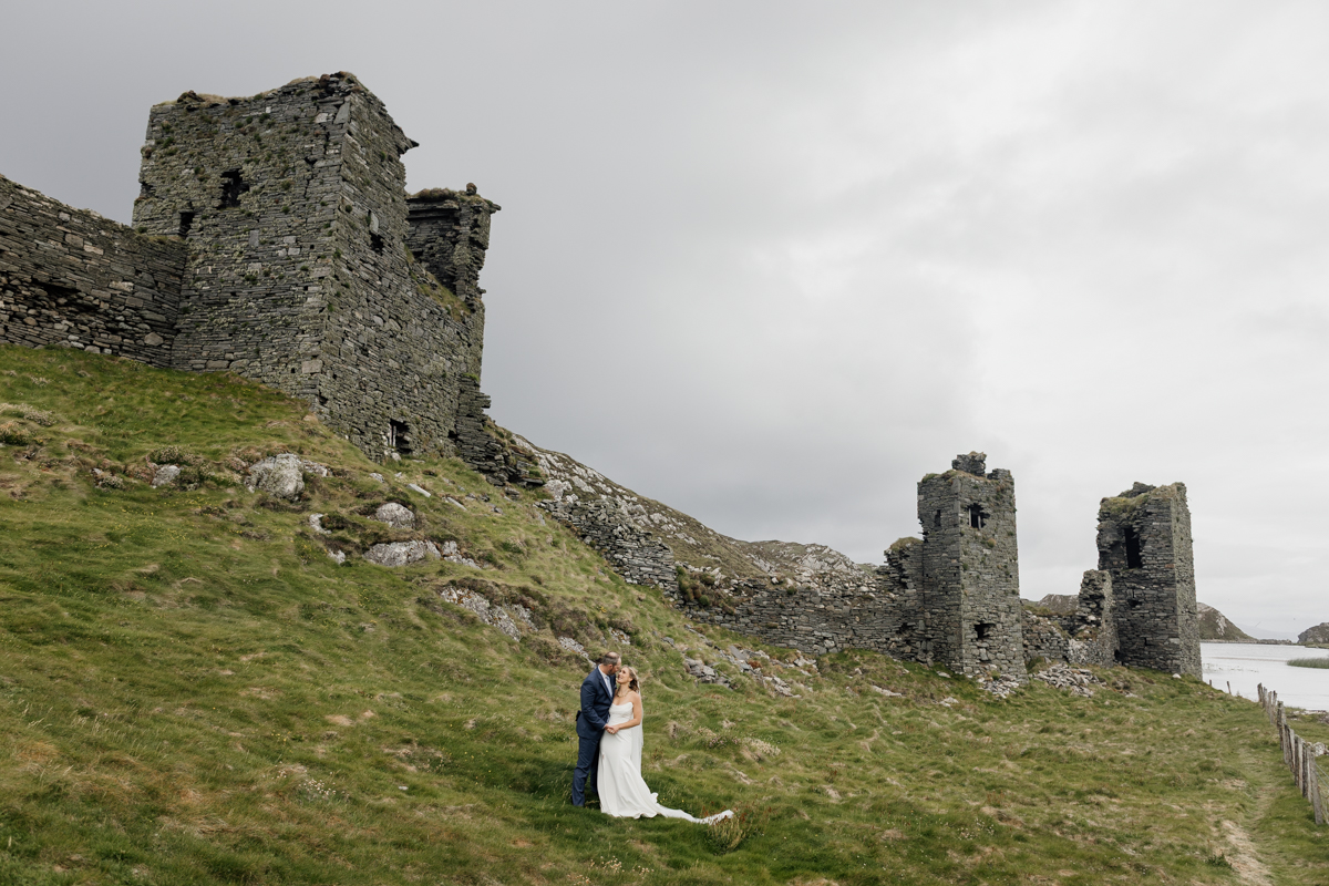 Bride and groom walking hand in hand at Three Castle Head ruins overlooking the Atlantic, Mizen Head, County Cork, Ireland elopement.